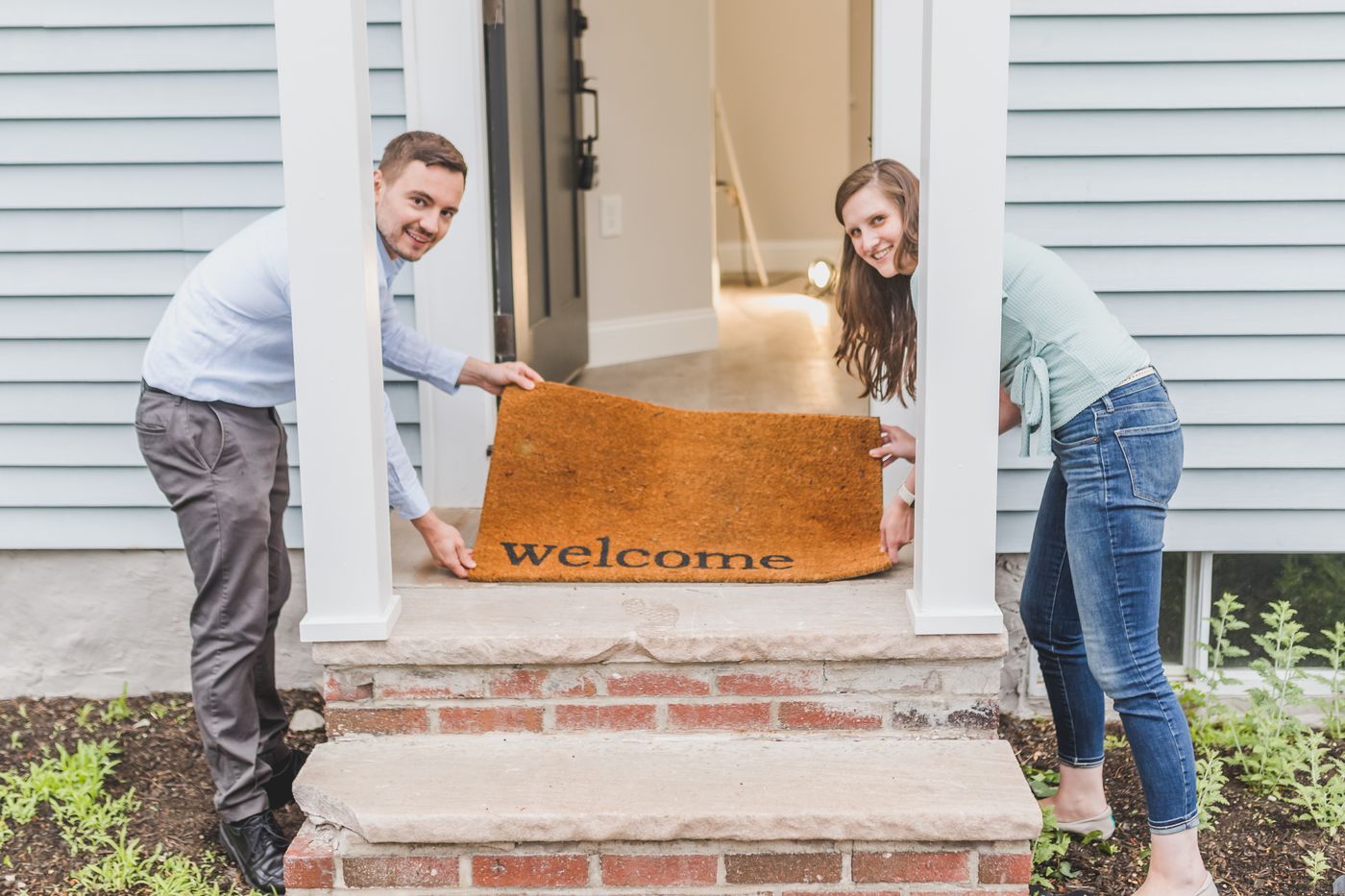 Two people holding a welcome doormat